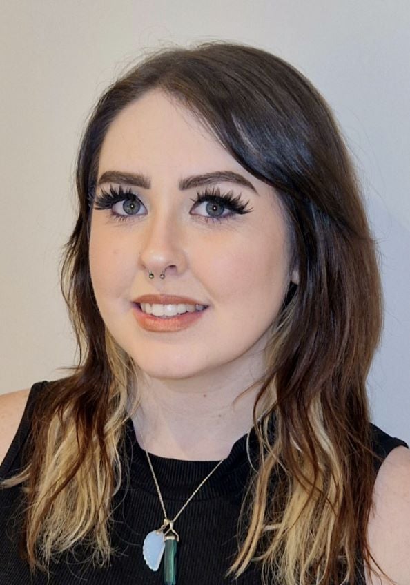 Smiling woman with long dark hair, wearing a sleeveless black top, against a neutral background.